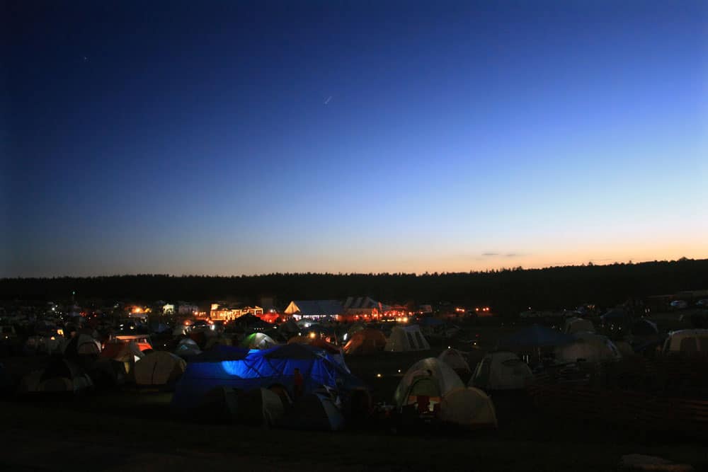 Tents are set up in a field as the sky transitions from dusk to night.