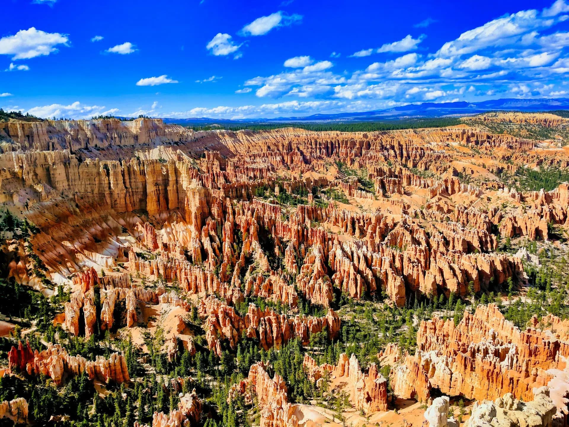 A panoramic view of Bryce Canyon's vibrant orange hoodoos under a bright blue sky with scattered clouds.
