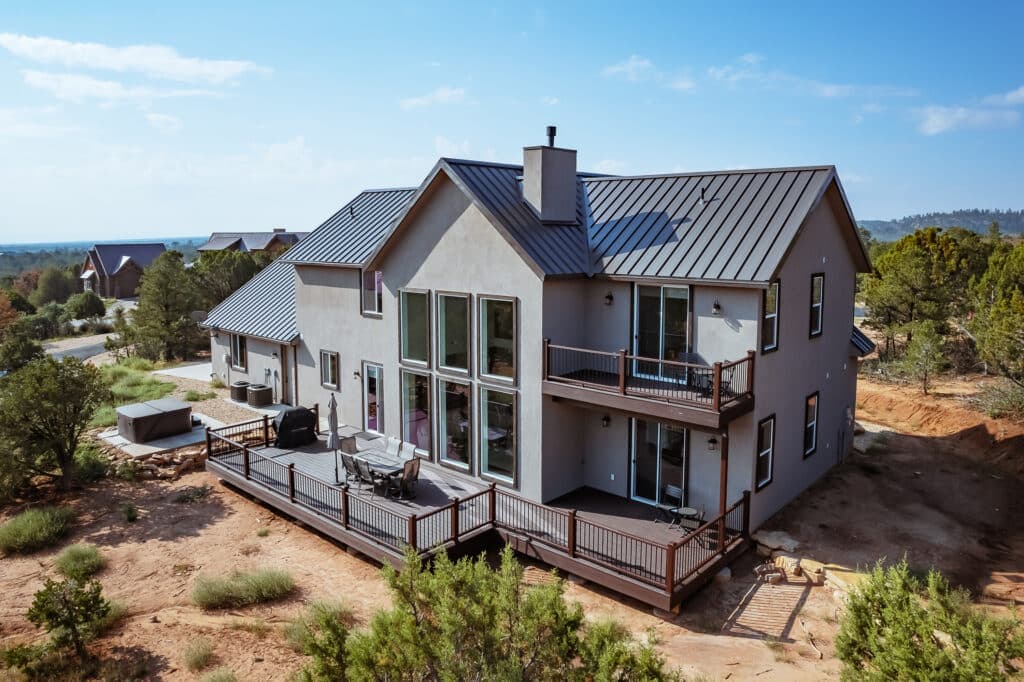 A modern two-story house with a metal roof and a large deck surrounded by greenery.