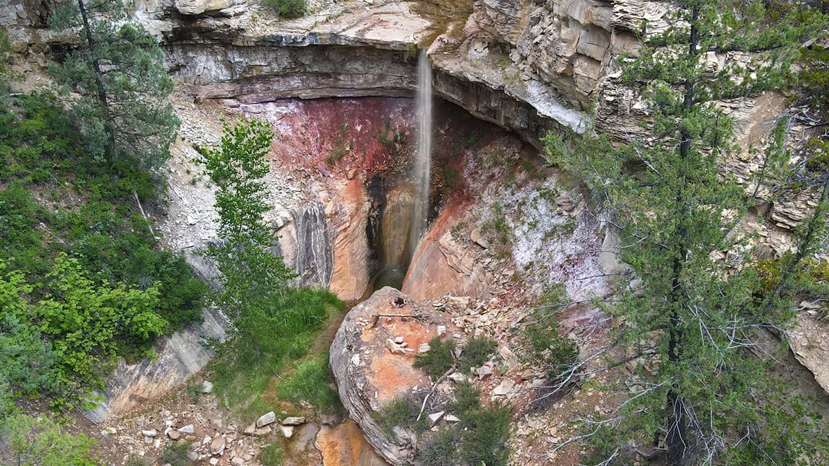 A waterfall cascades into a colorful canyon surrounded by lush greenery.