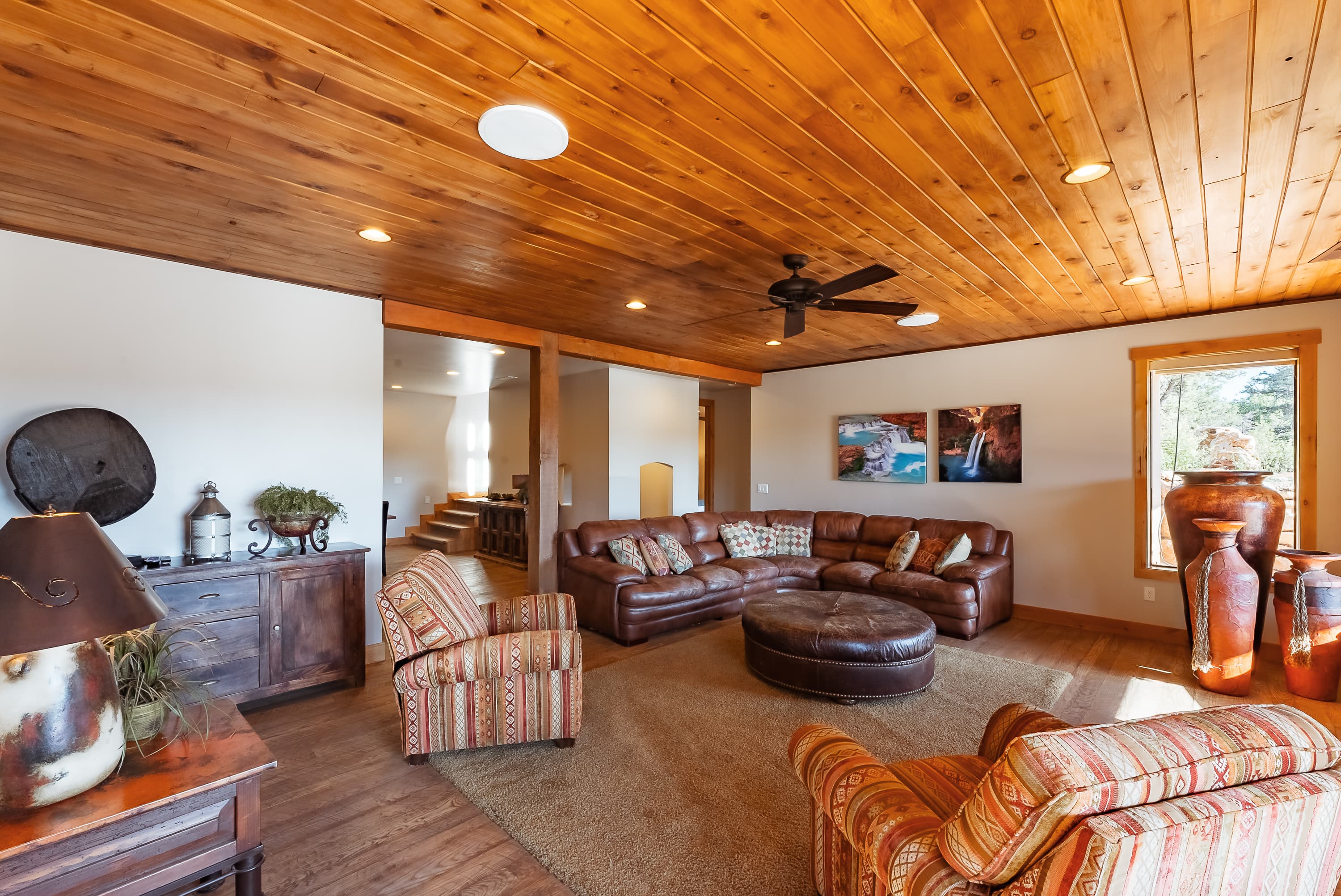 Cozy living room featuring a leather sectional, striped chairs, wooden ceiling, and decorative vases.