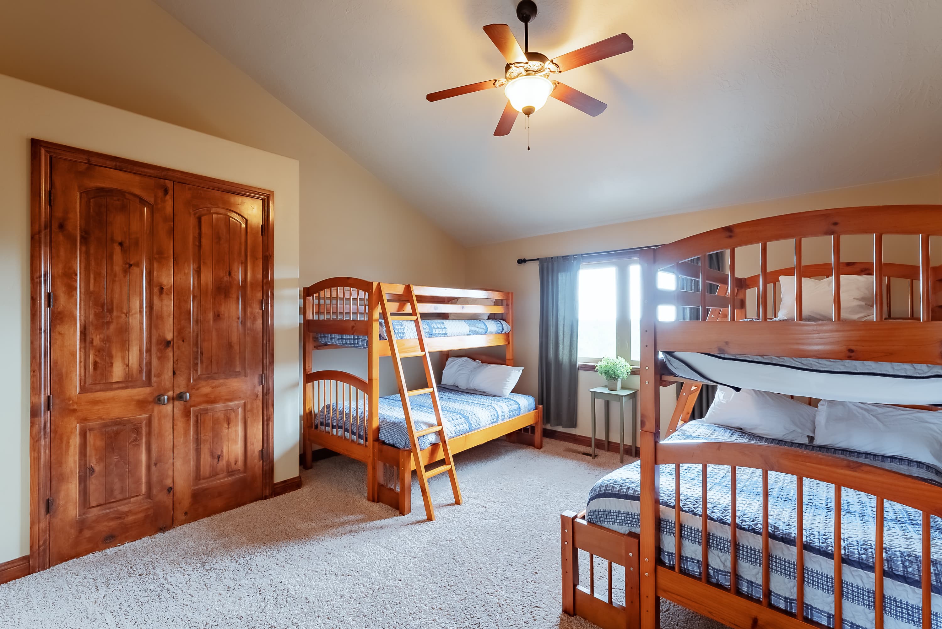 A cozy bedroom featuring two wooden bunk beds, a ceiling fan, and natural light from a window.