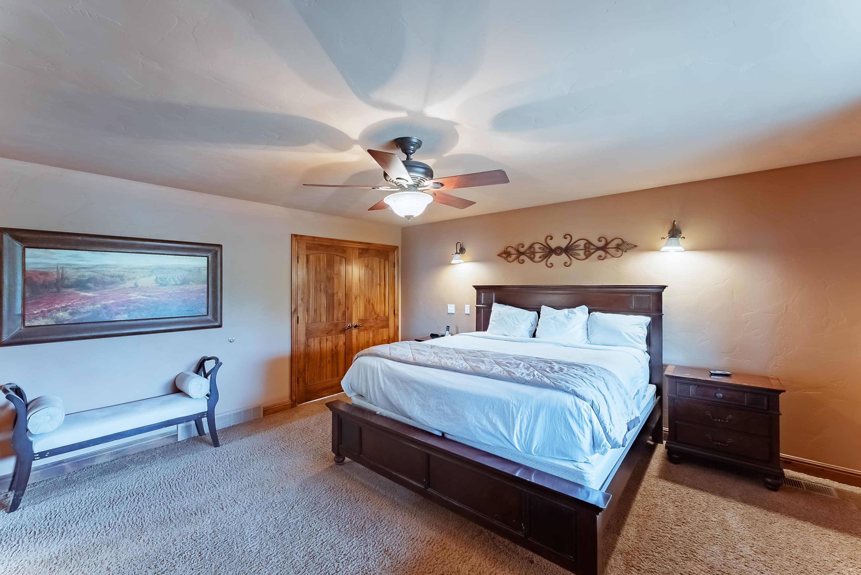 A cozy bedroom featuring a king-sized bed, a bench, and wooden accents.
