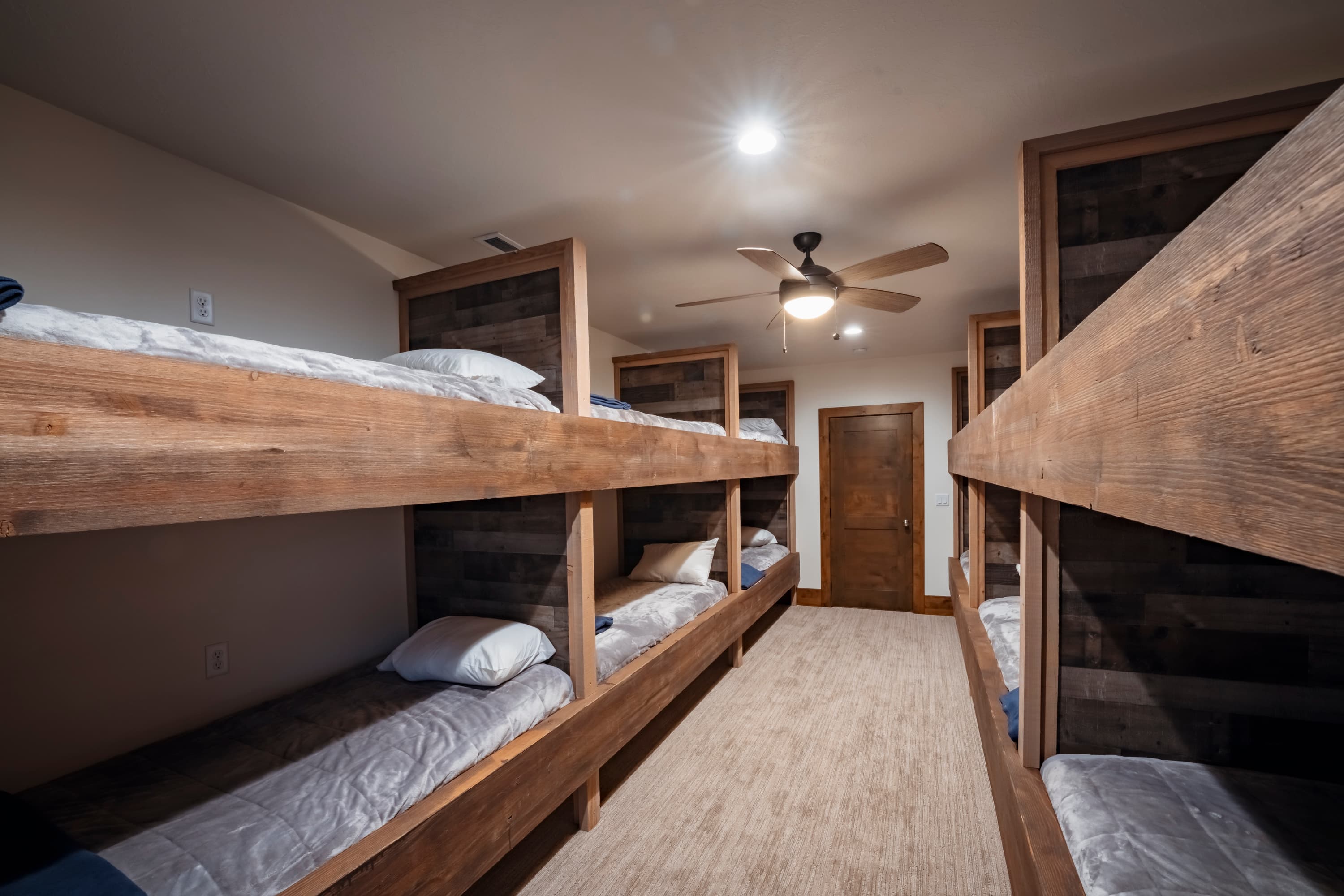 A cozy room featuring wooden bunk beds with mattresses and a ceiling fan.