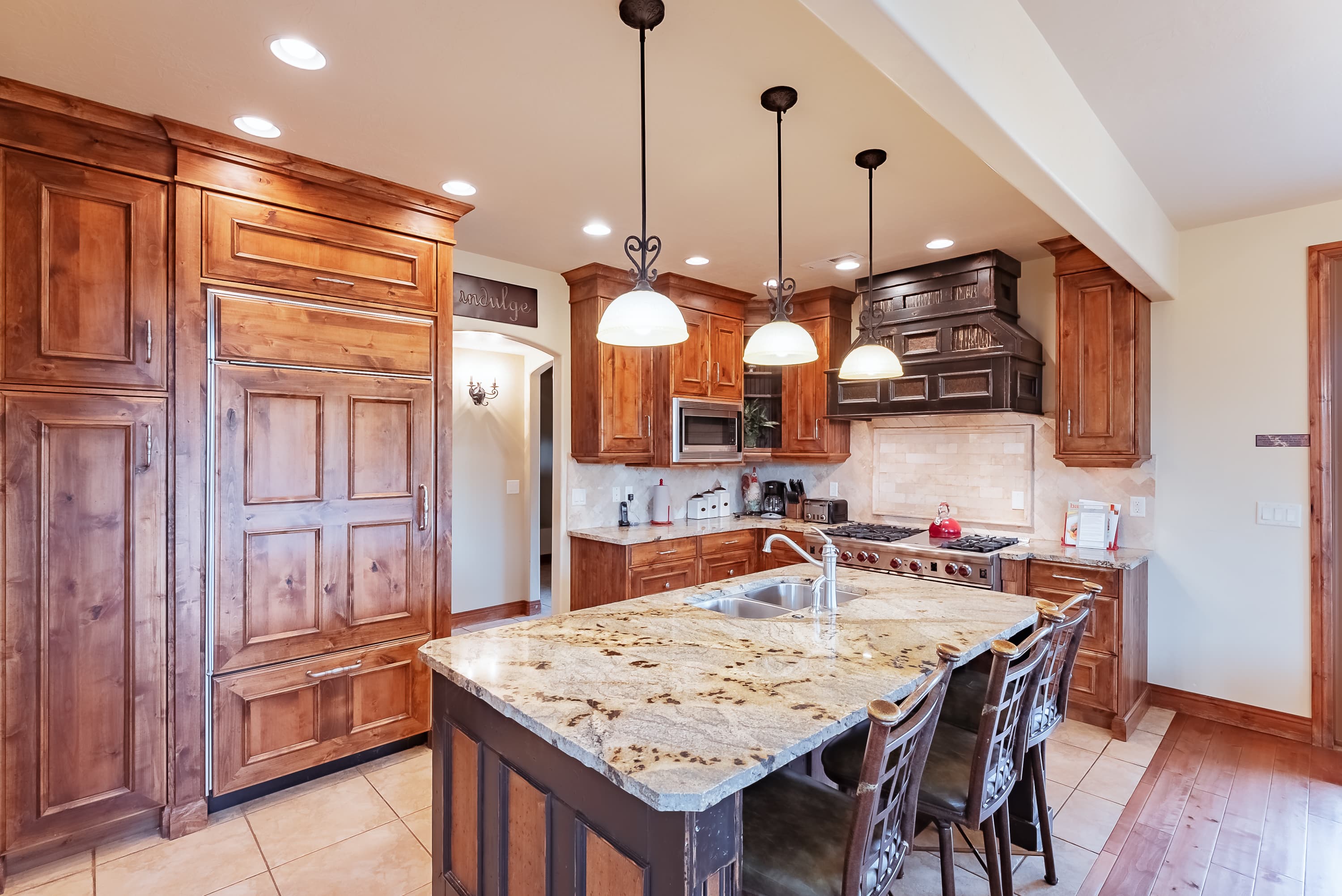 Modern kitchen with wooden cabinetry, granite island, and pendant lighting.