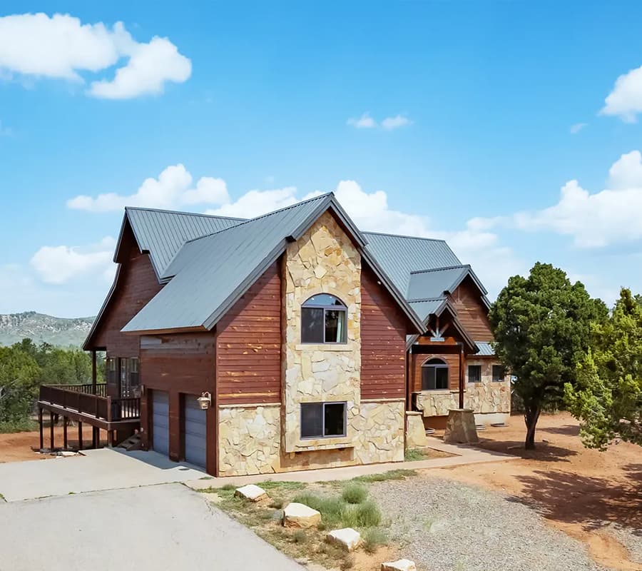 A modern two-story house with a mix of wooden and stone exterior, set against a blue sky.
