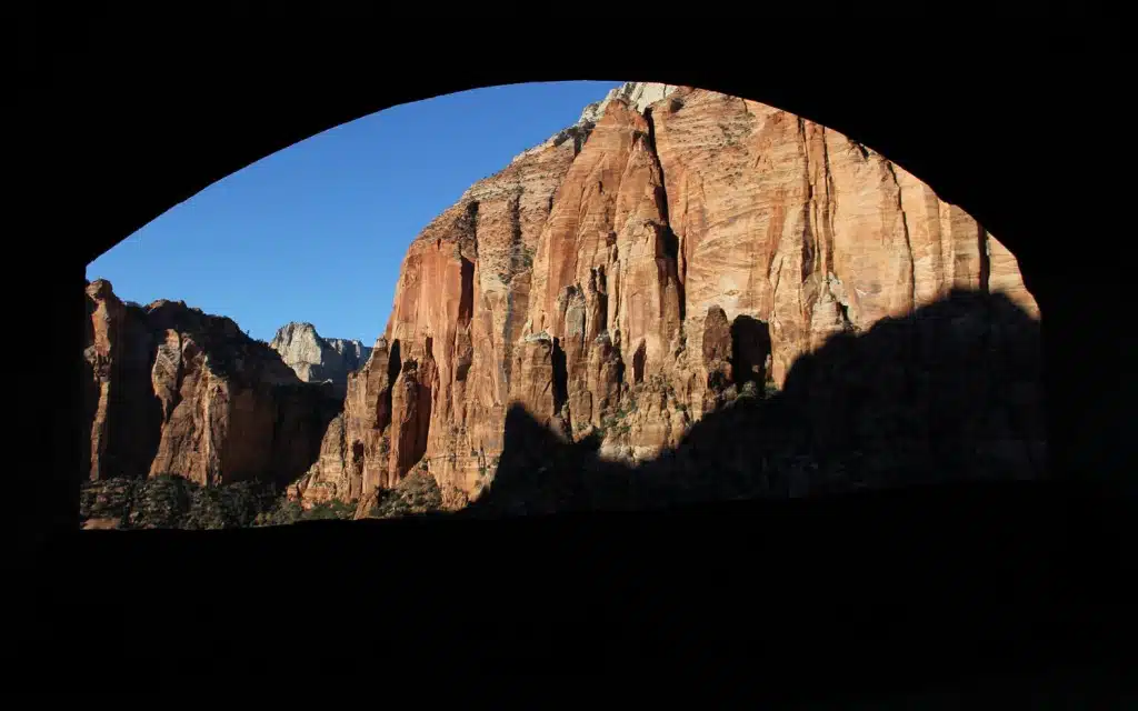View of towering red rock formations framed by an archway against a clear blue sky.