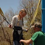 A young girl with braids prepares to jump on a bungee trampoline while an adult assists her.