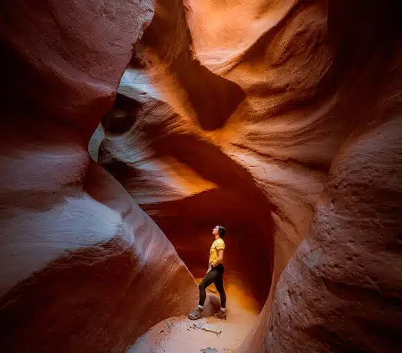 A person stands in a narrow, colorful canyon surrounded by smooth, twisted rock formations.