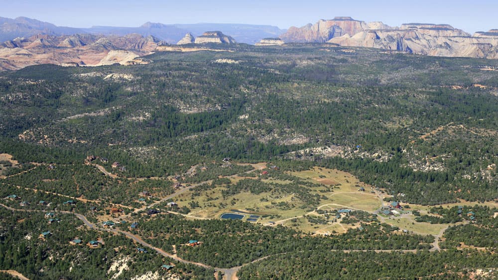 Aerial view of a vast landscape featuring rolling hills, scattered trees, and distant mountains.