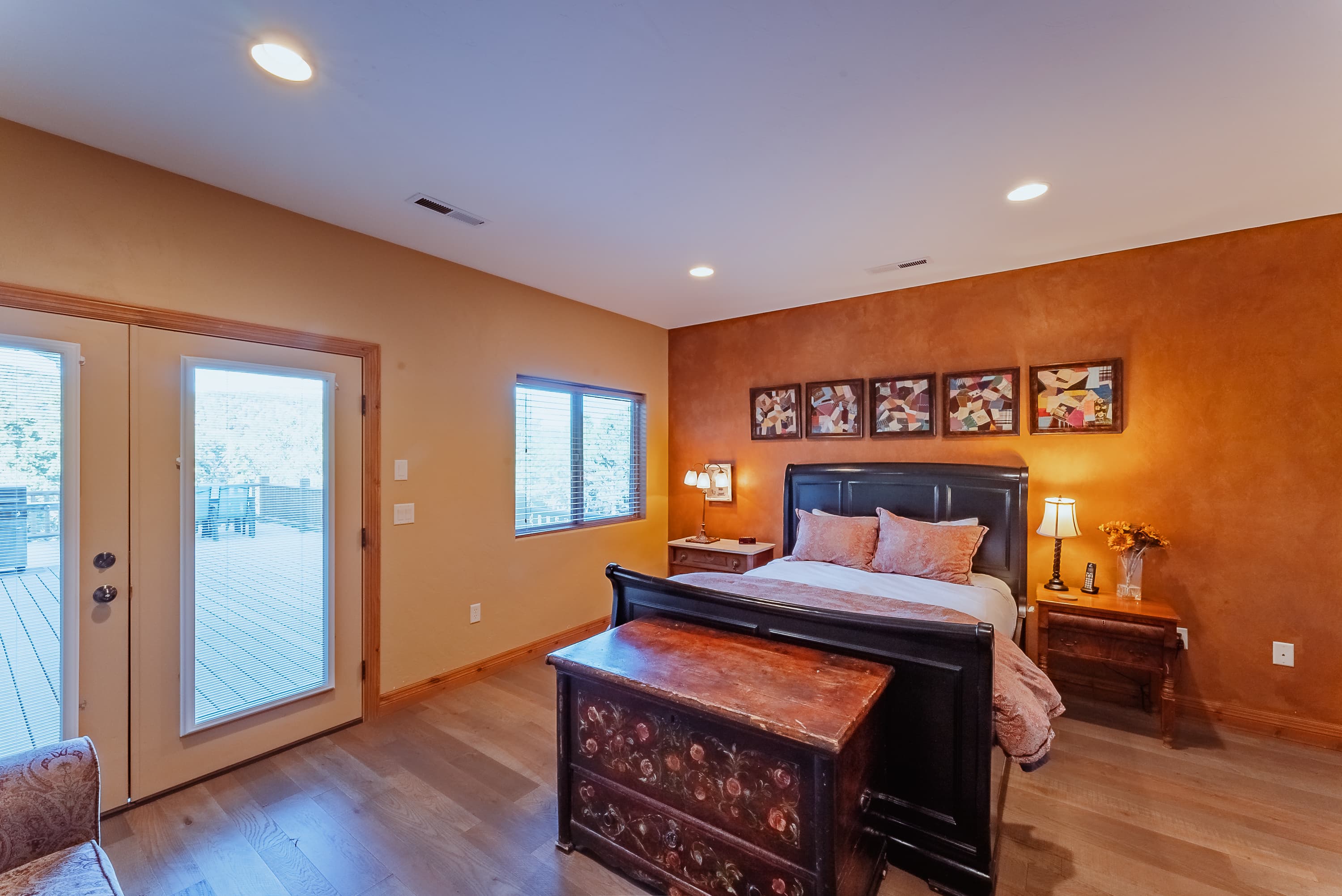 Cozy bedroom featuring a black bed, wooden furniture, and large windows leading to a deck.