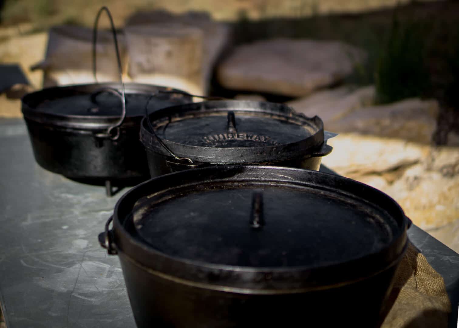 Three black cast iron Dutch ovens sit on a metallic surface.