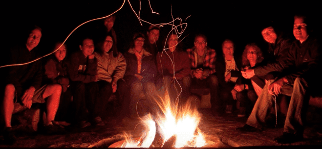A group of people gathered around a glowing campfire at night.
