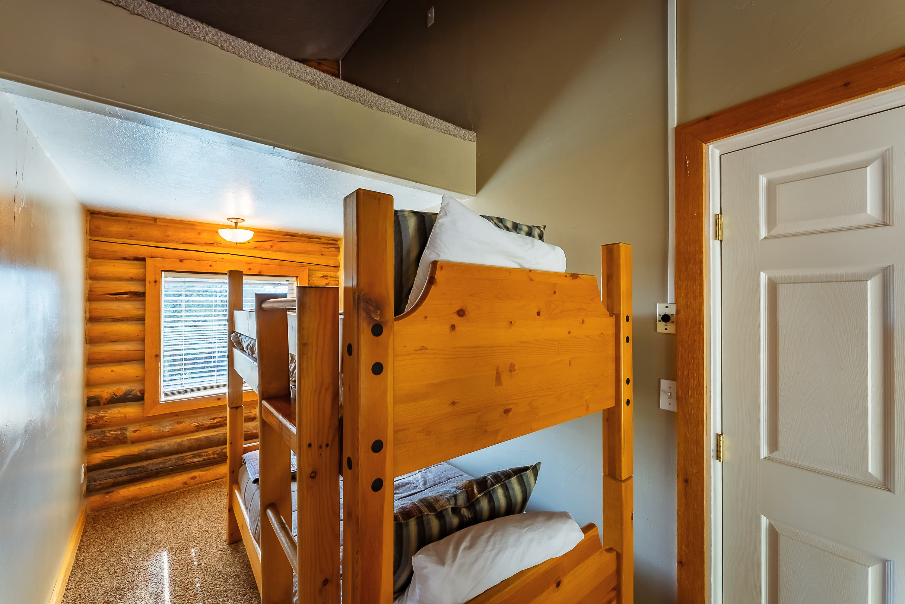 Bunk beds in a cozy, log cabin bedroom with a window and light fixture.