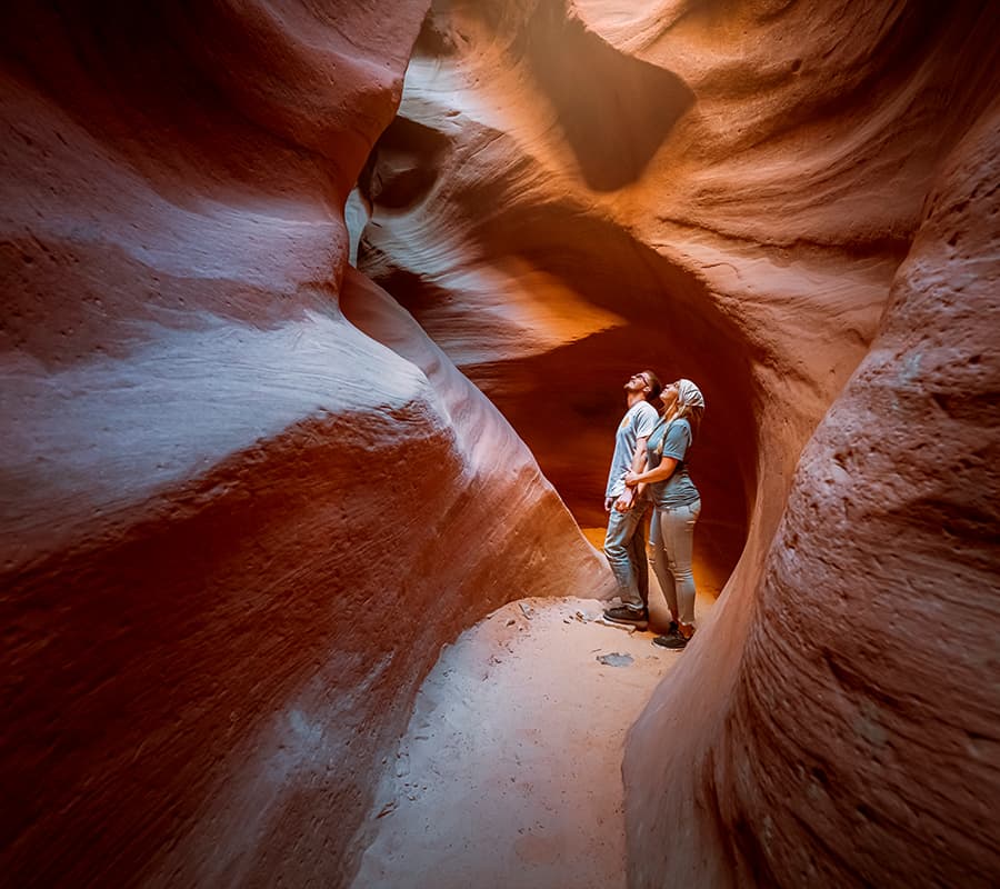 A couple admires the natural beauty of a narrow, red sandstone canyon.