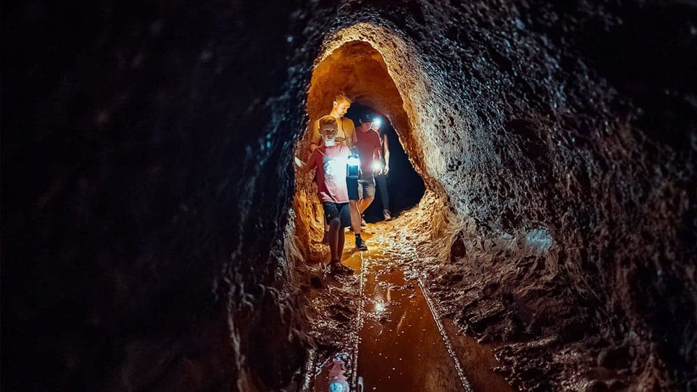 Two people explore a narrow, dark cave illuminated by flashlights.