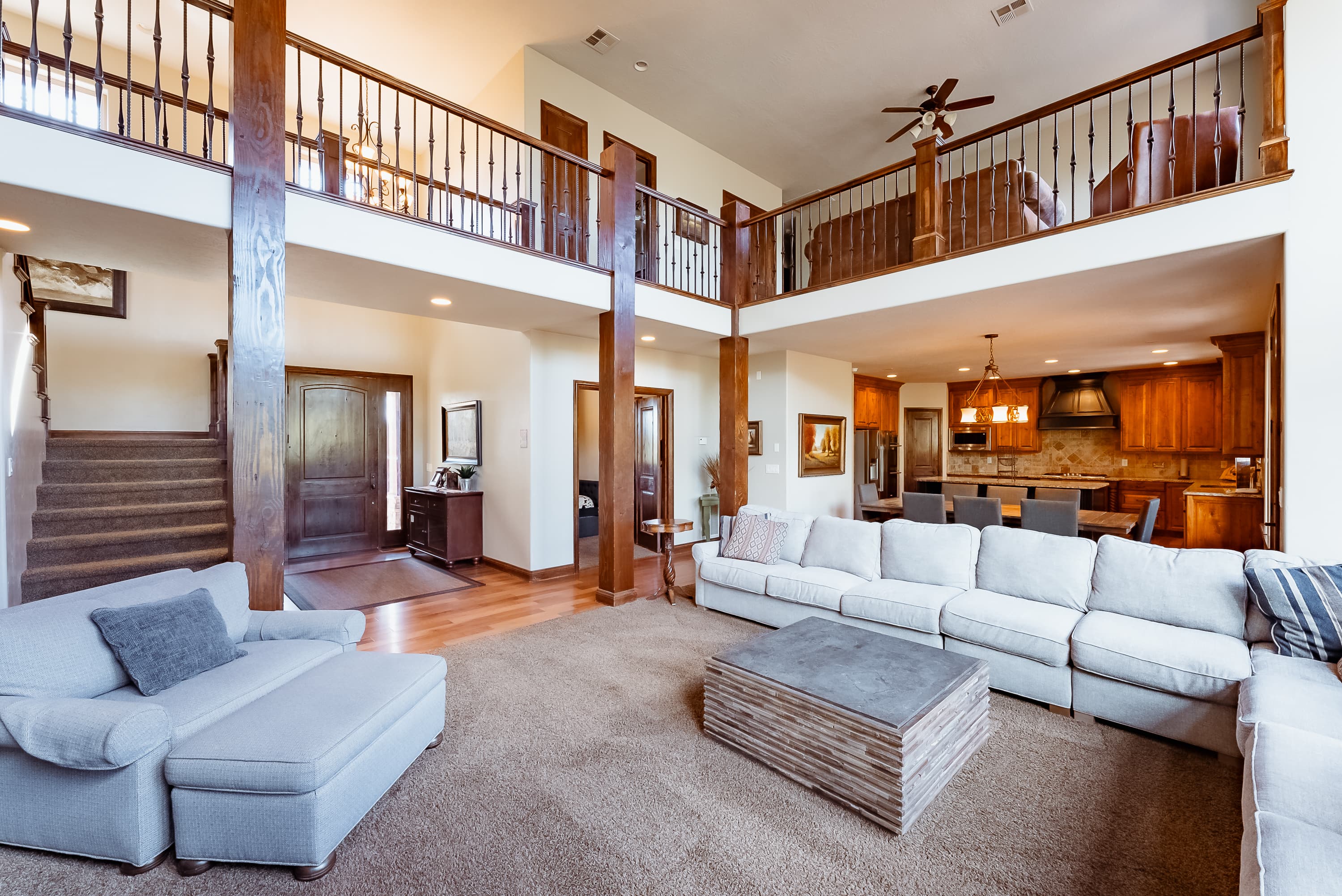 A spacious, two-story living room featuring a large sectional sofa, a wooden coffee table, and access to a modern kitchen and dining area.