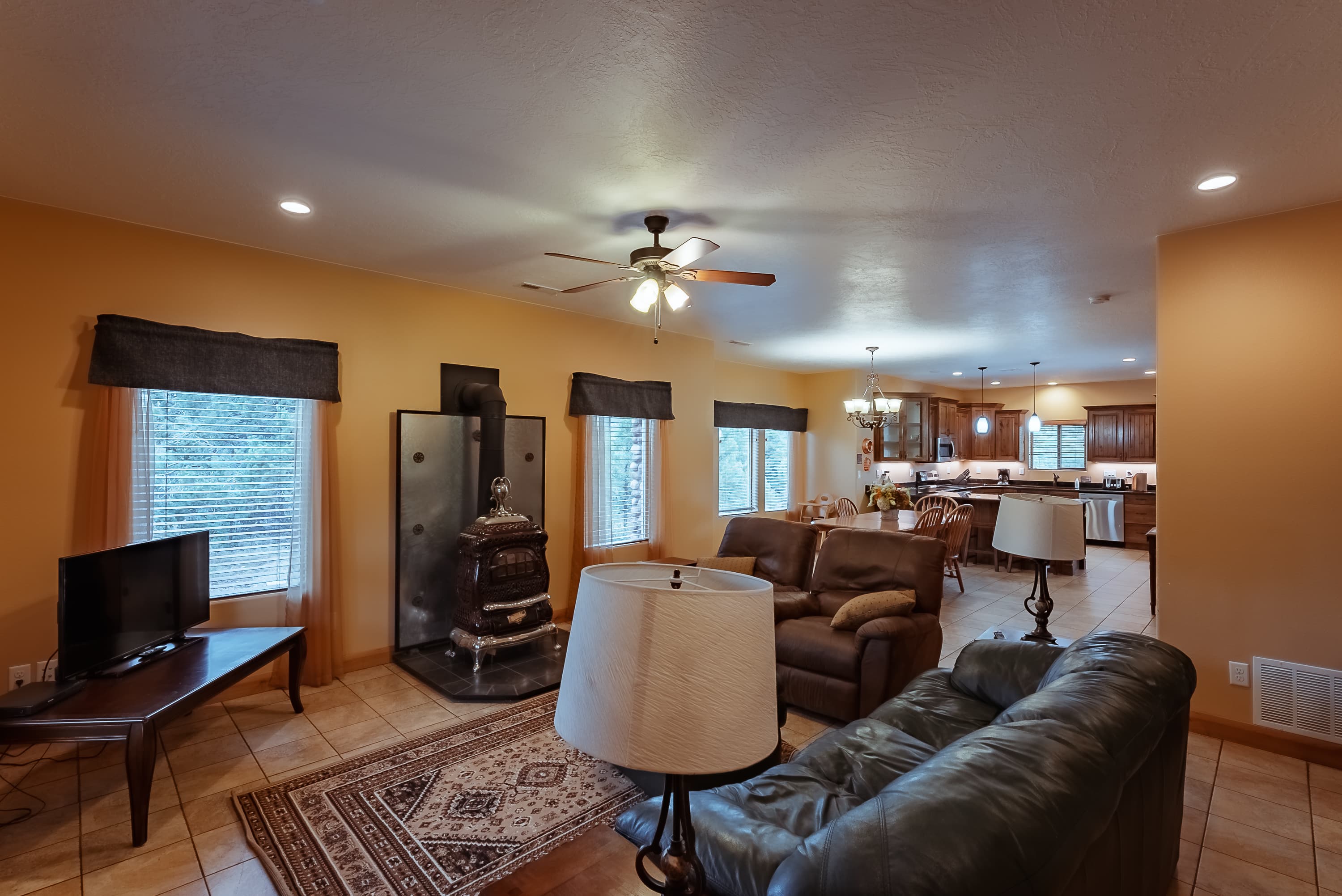 Cozy living room featuring a leather couch, coffee table, TV, and visible kitchen area with wood cabinets.