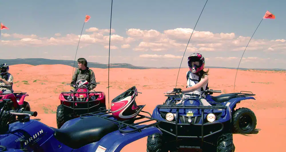 Two individuals on ATVs in a sandy desert landscape.