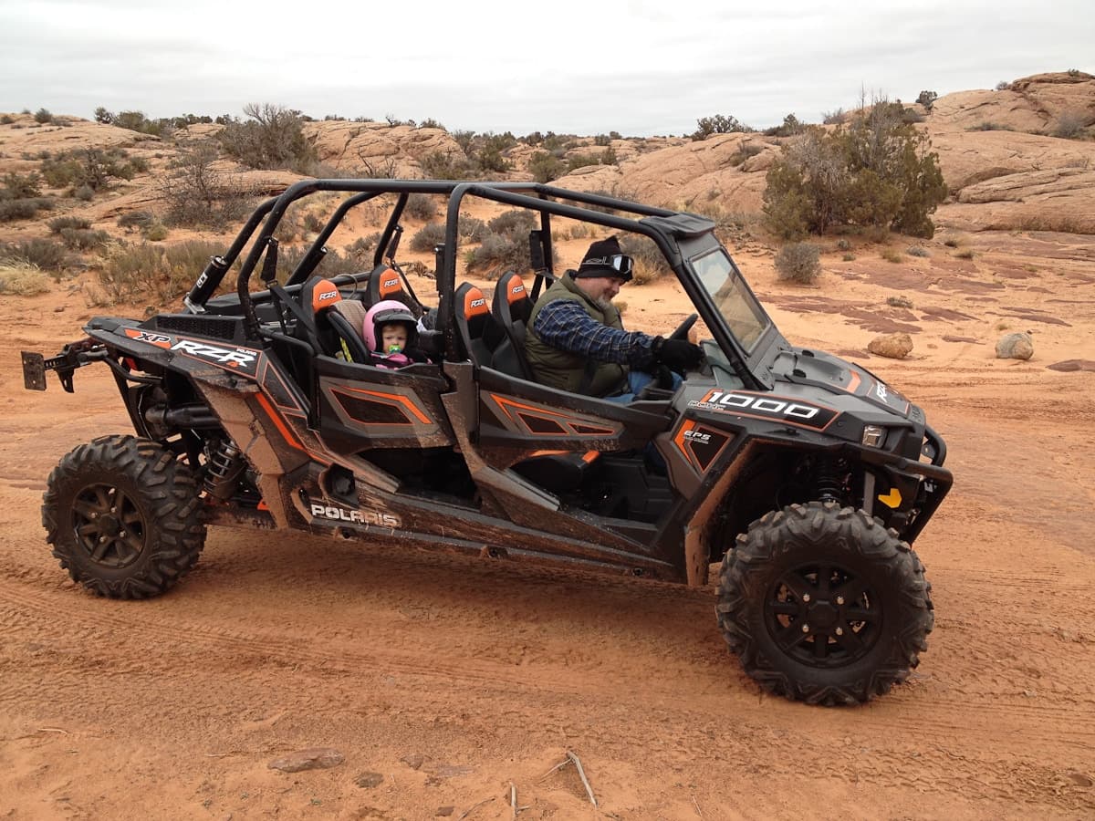 A man and a child sit in an off-road vehicle on a sandy terrain.