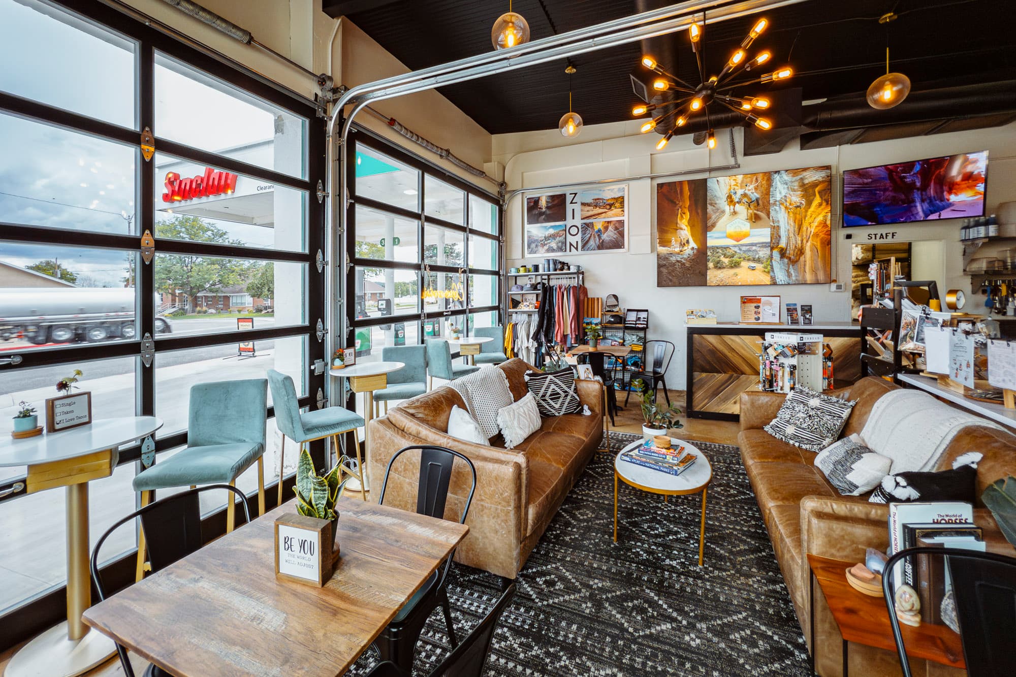 A cozy café interior featuring leather sofas, artistic decor, and large windows opening to the street.