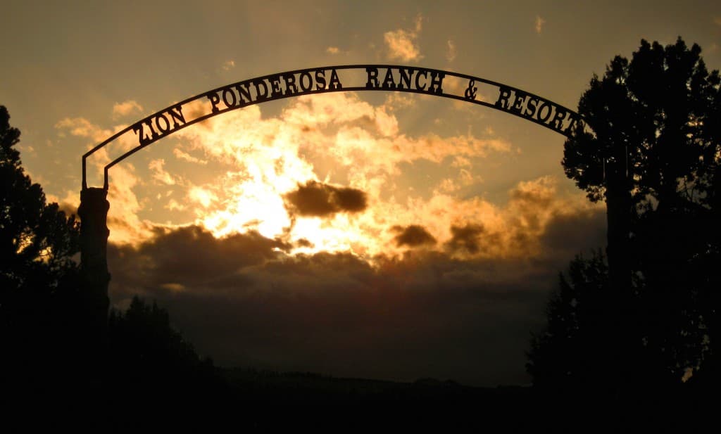 The silhouette of a sign for Zion Ponderosa Ranch & Resort against a dramatic sunset sky.