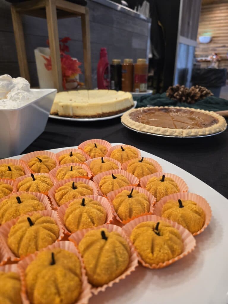 A platter of decorative pumpkin-shaped desserts in front of various pies and treats on a table.