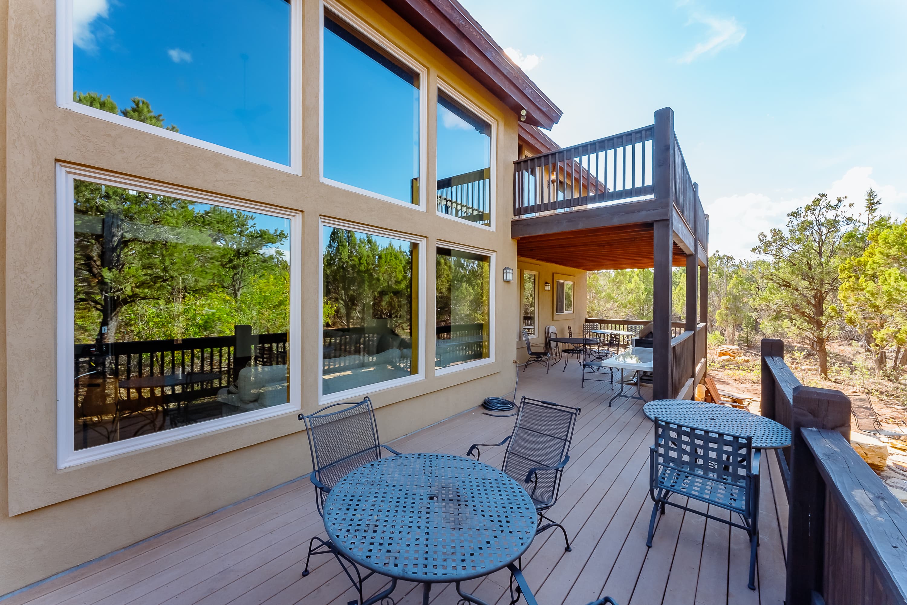 A spacious outdoor deck with metal tables and chairs, overlooking trees and blue skies.