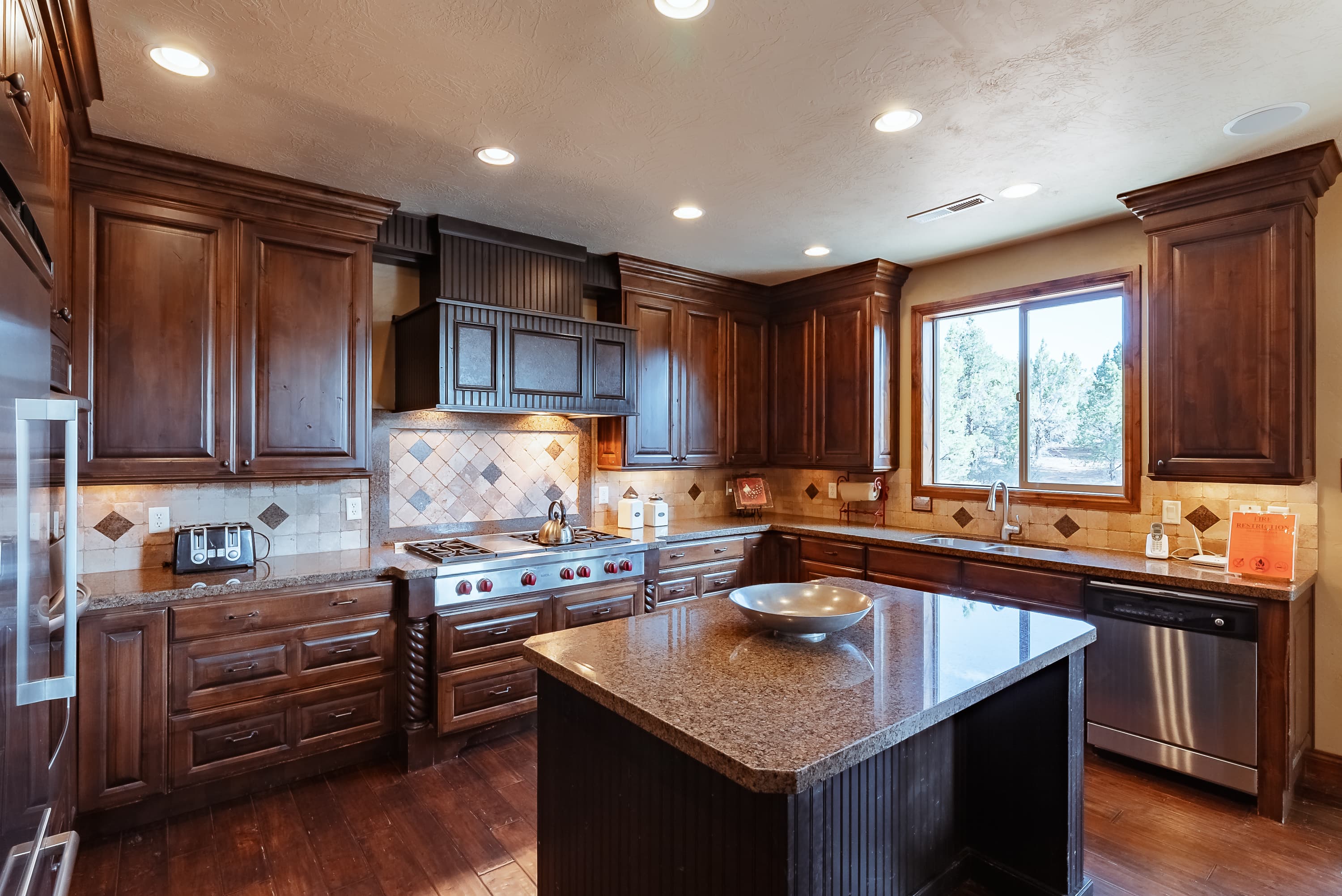 Modern kitchen featuring dark wood cabinets, granite island, and stainless steel appliances.