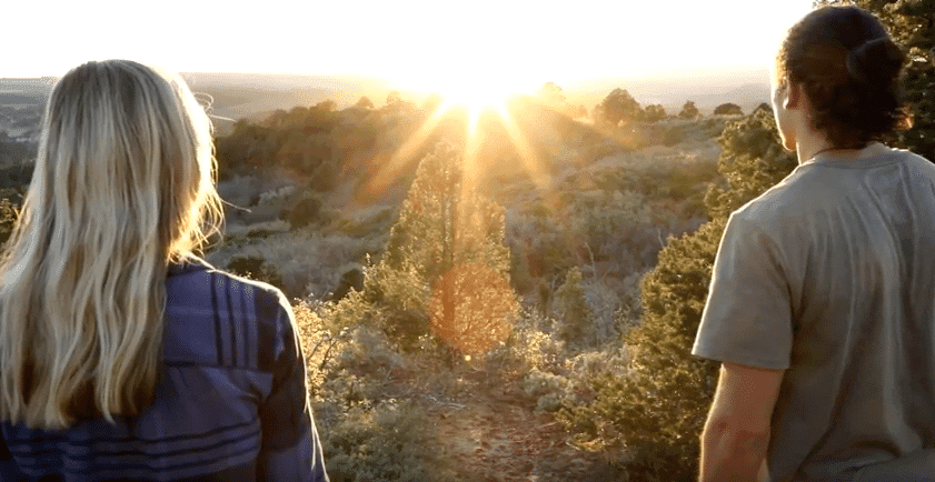 Two people watch the sunset over a scenic landscape.