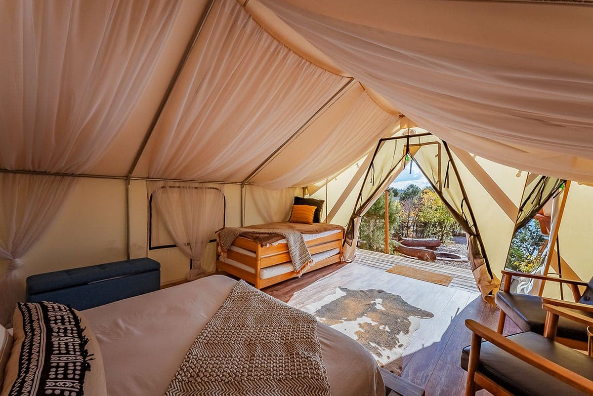 Interior of a spacious glamping tent with two beds and a view of nature.
