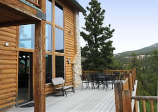 A wooden deck with outdoor seating and large windows overlooking a mountainous landscape.