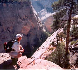A hiker crouches on a rocky ledge overlooking a vast canyon.