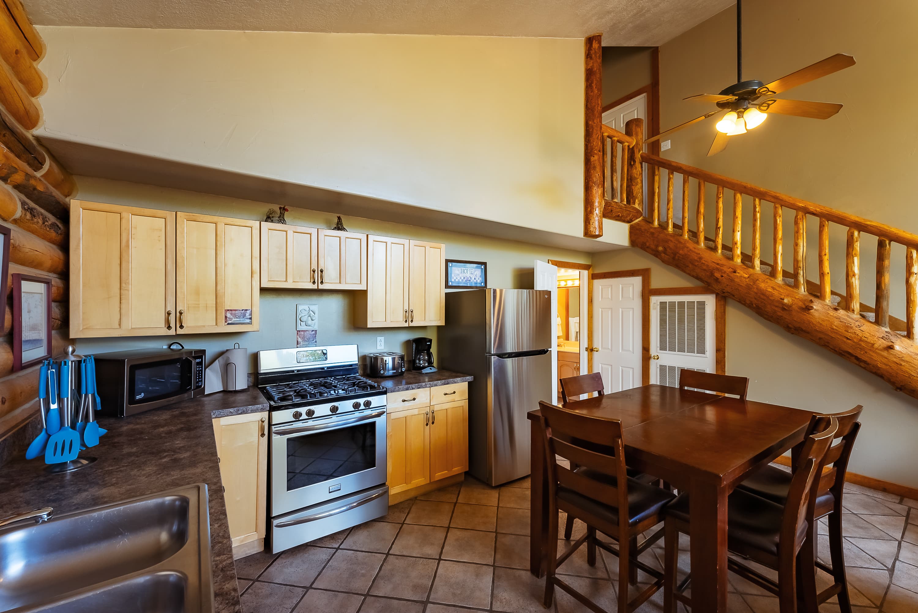 Modern kitchen with wooden cabinetry, stainless steel appliances, and a dining table in a log cabin setting.