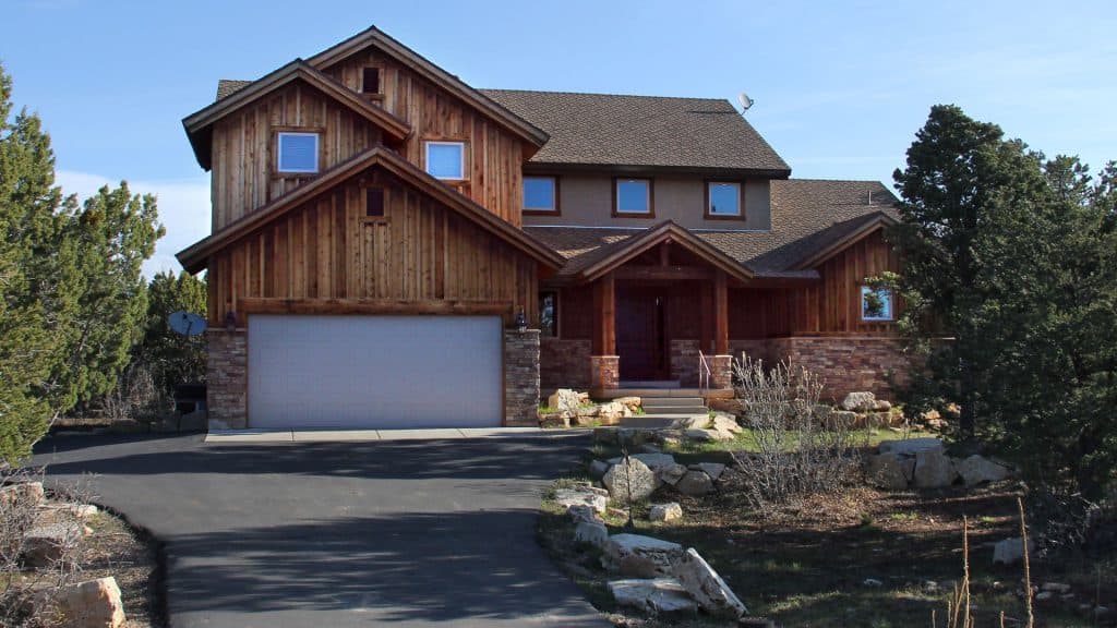 A large wooden house with multiple gables and a stone garage, surrounded by trees and shrubs.