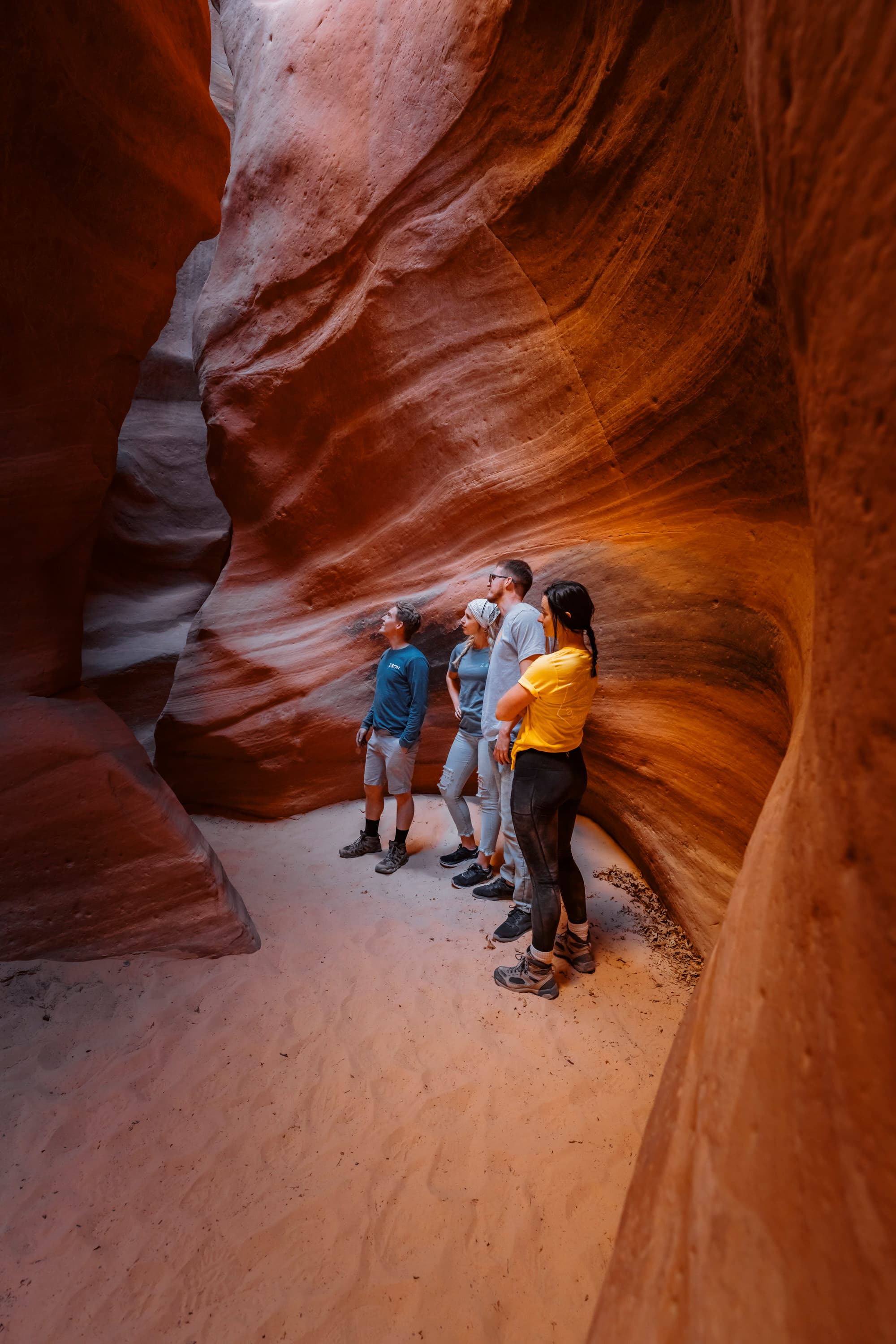 A group of four people stands in a narrow, vividly colored canyon, looking up in awe.