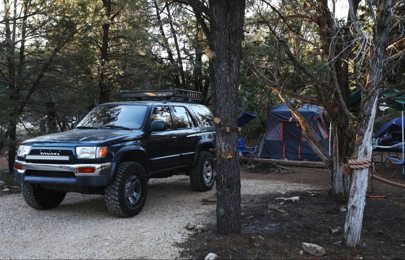 A black SUV parked near a campsite surrounded by trees and a tent.