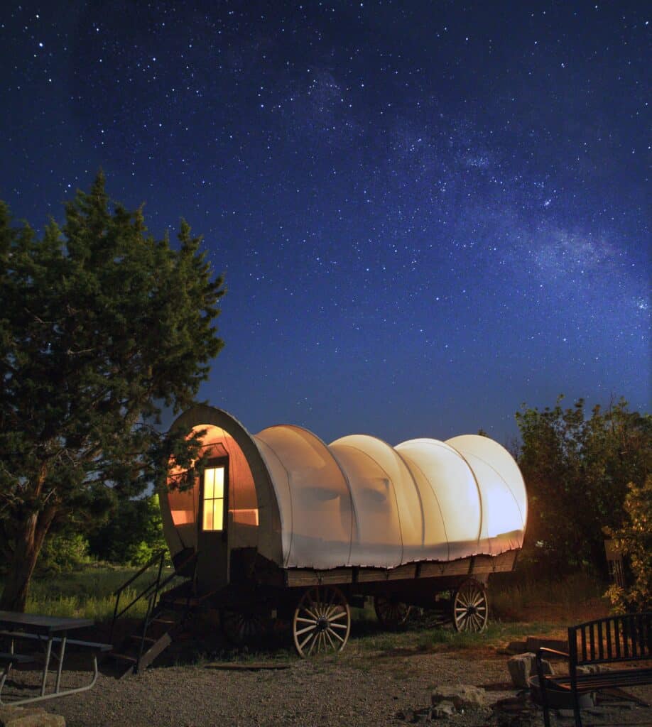 A vintage wagon under a starry night sky with a hint of warm light from its window.