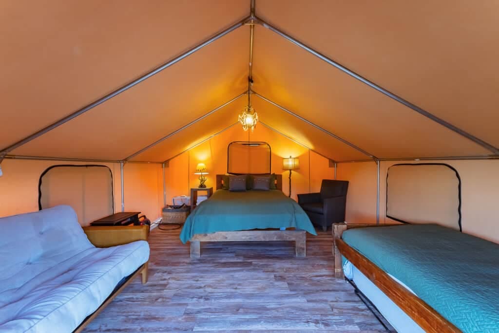 Interior view of a spacious tent with a bed, seating area, and warm lighting.