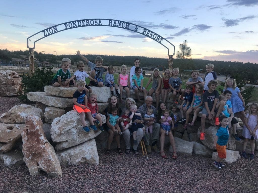 A large group of children and several adults pose together on rocks under the "Ponderosa Ranch & Resort" sign at sunset.