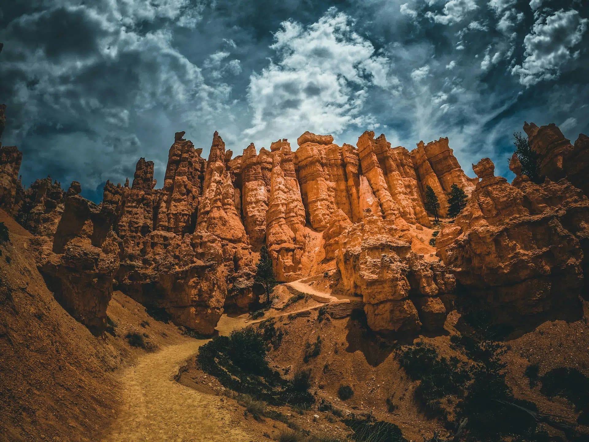 A winding path leads through towering orange rock formations under a dramatic sky.