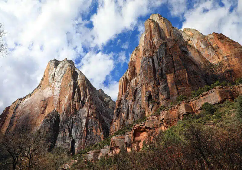 Majestic red rock cliffs rise against a blue sky with scattered clouds.