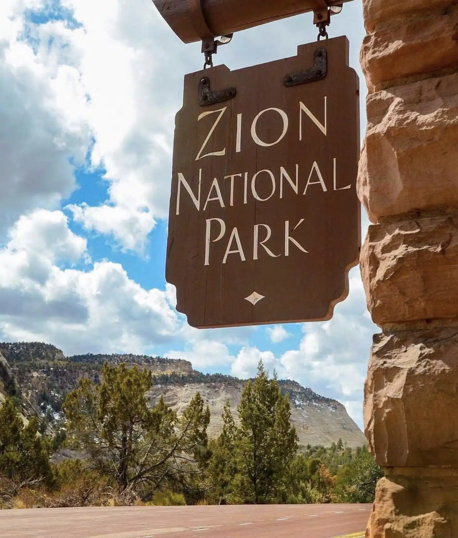 Sign for Zion National Park with scenic landscape in the background.