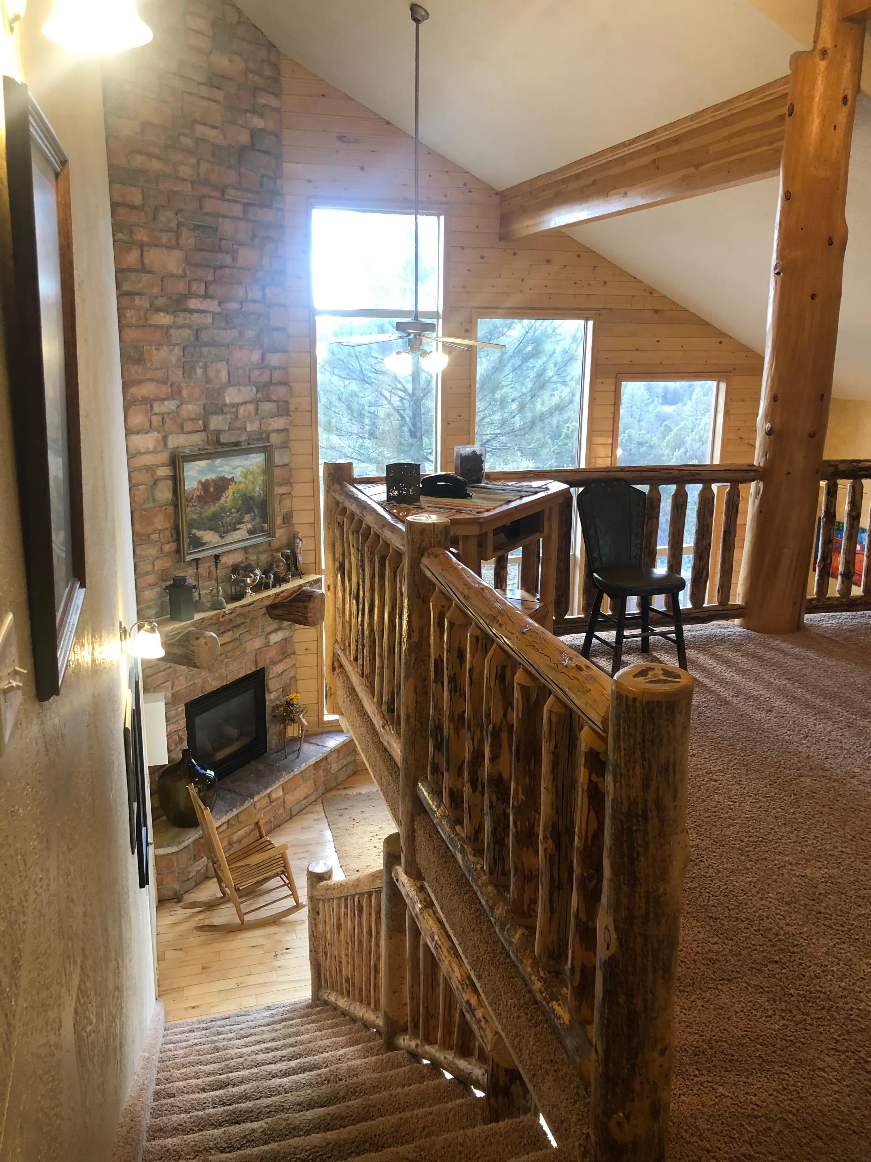 A wooden staircase leads to a spacious, rustic living area with large windows and a stone fireplace.