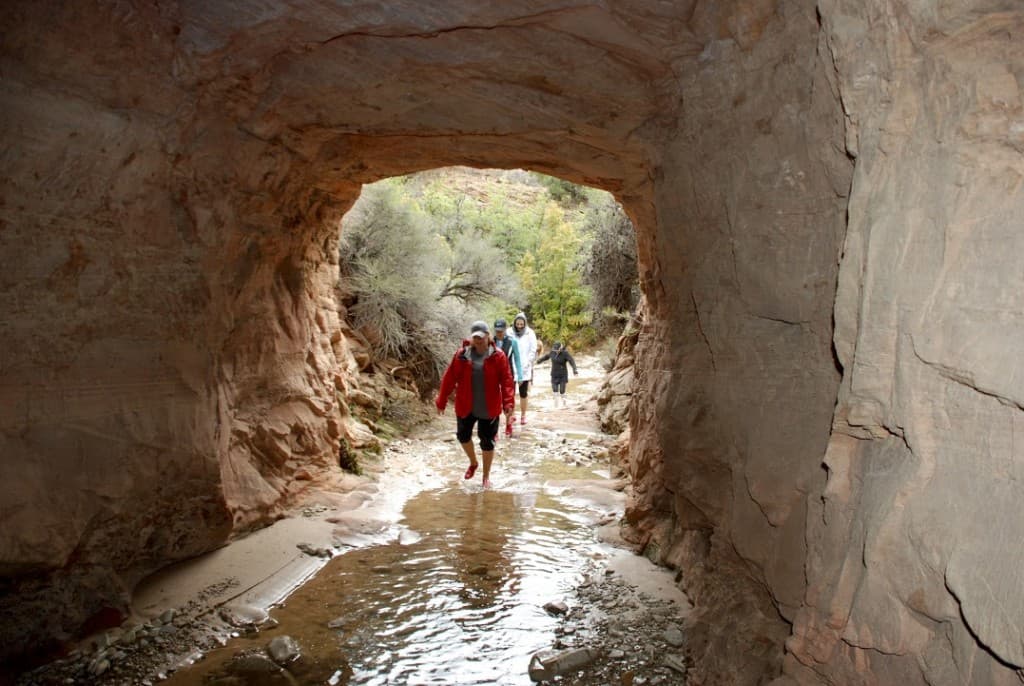 People walking through a rocky passageway with water on the ground.