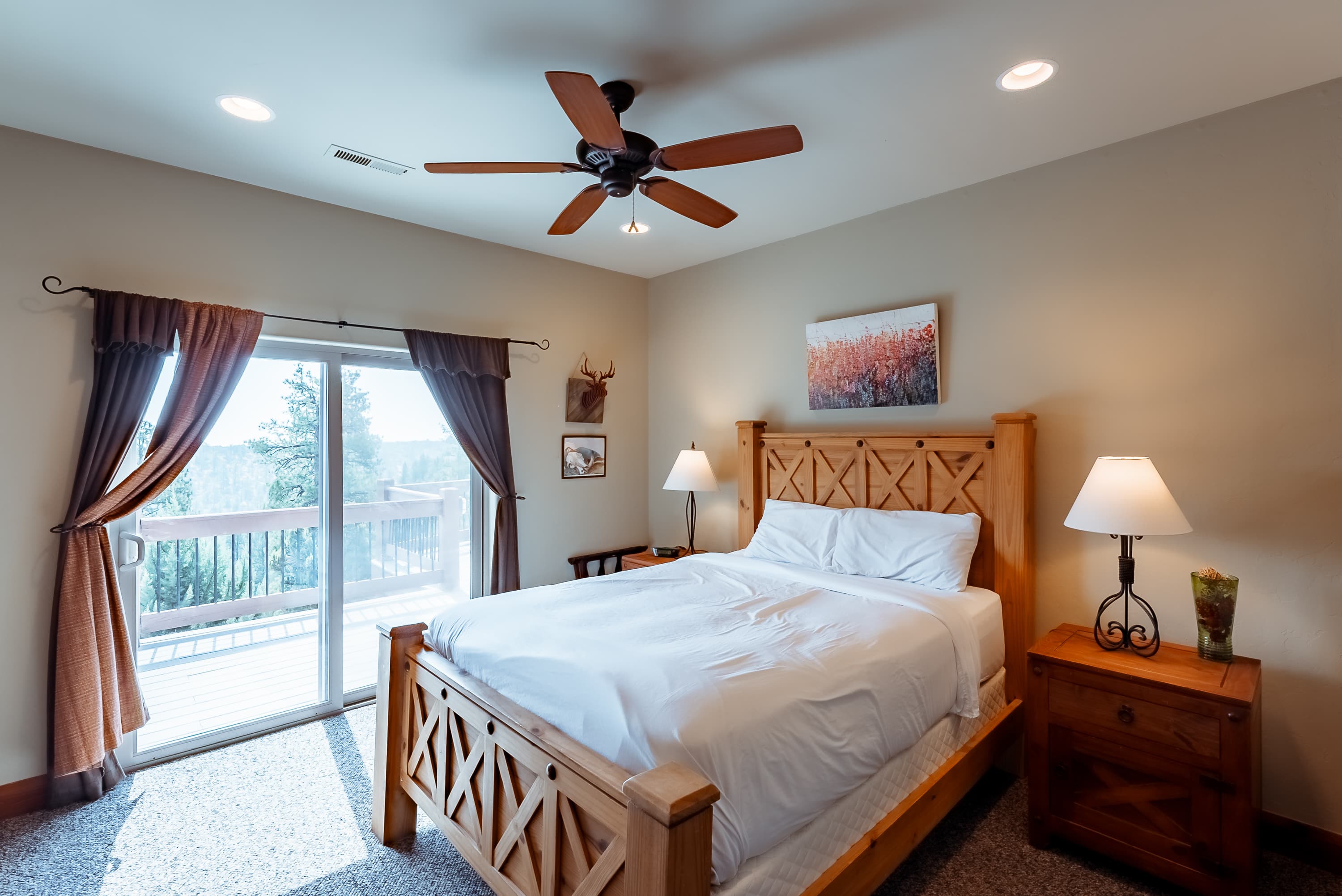 Cozy bedroom with a wooden bed, bedside lamps, and sliding glass door leading to a deck.