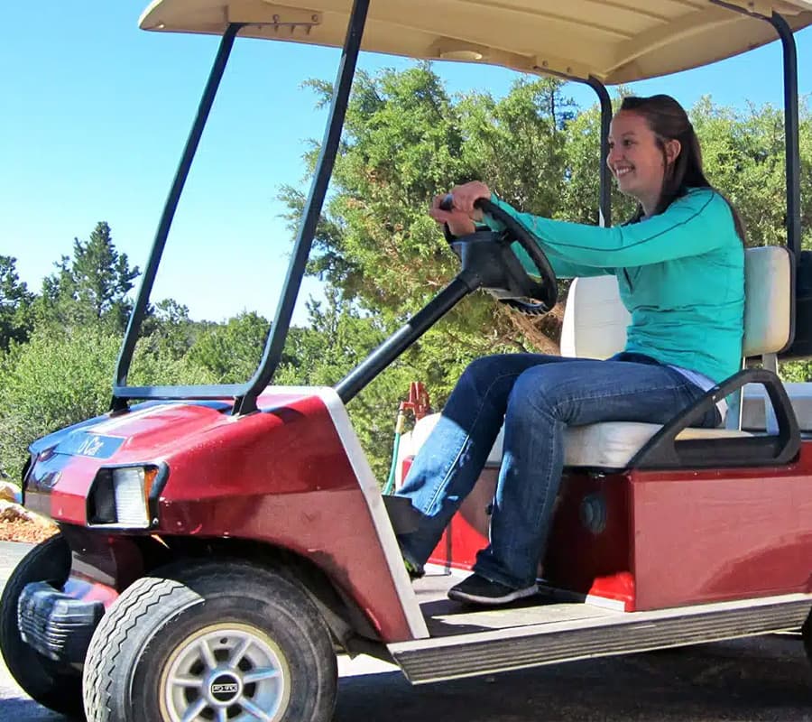 A woman smiles while driving a red golf cart on a sunny day.