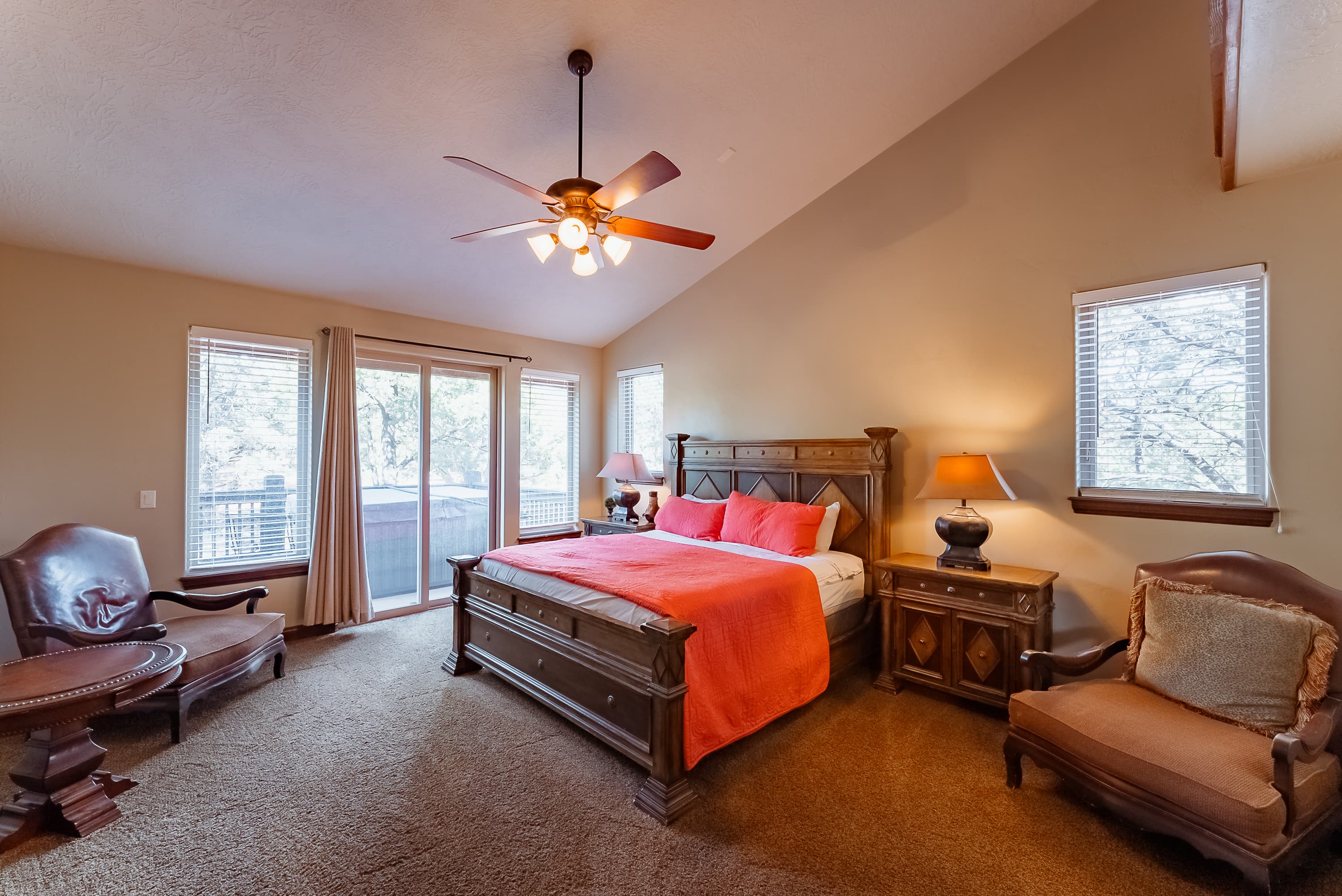Cozy bedroom featuring a wooden bed with an orange blanket, armchairs, and large windows.