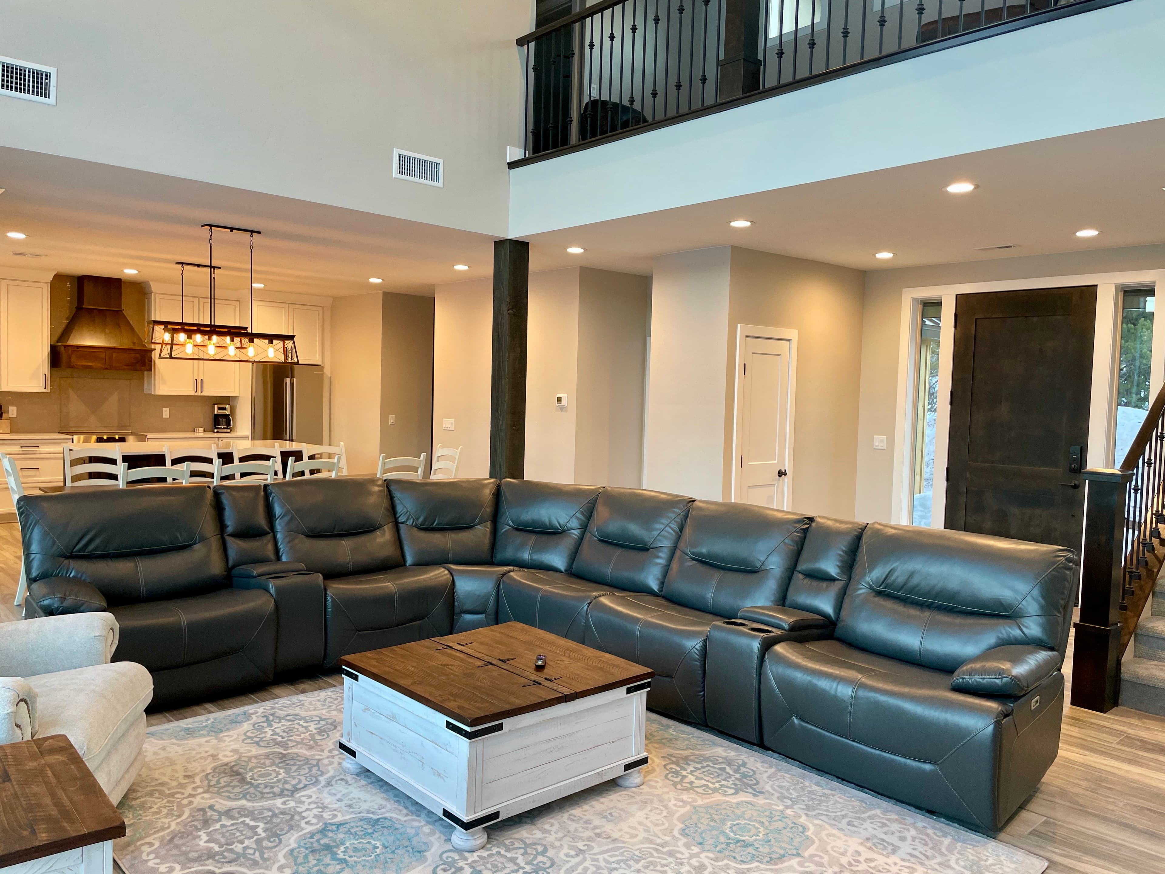 A spacious living room featuring a large dark leather sectional sofa and a wooden coffee table on a decorative rug.