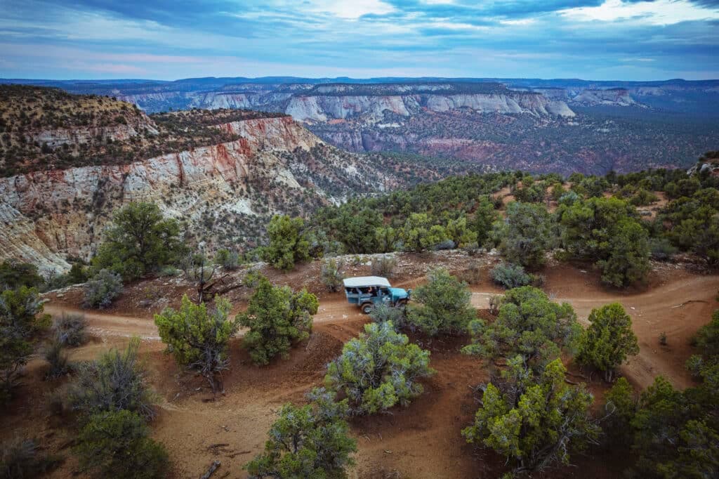 A blue vehicle parked on a dirt road amidst a rugged landscape of cliffs and trees.